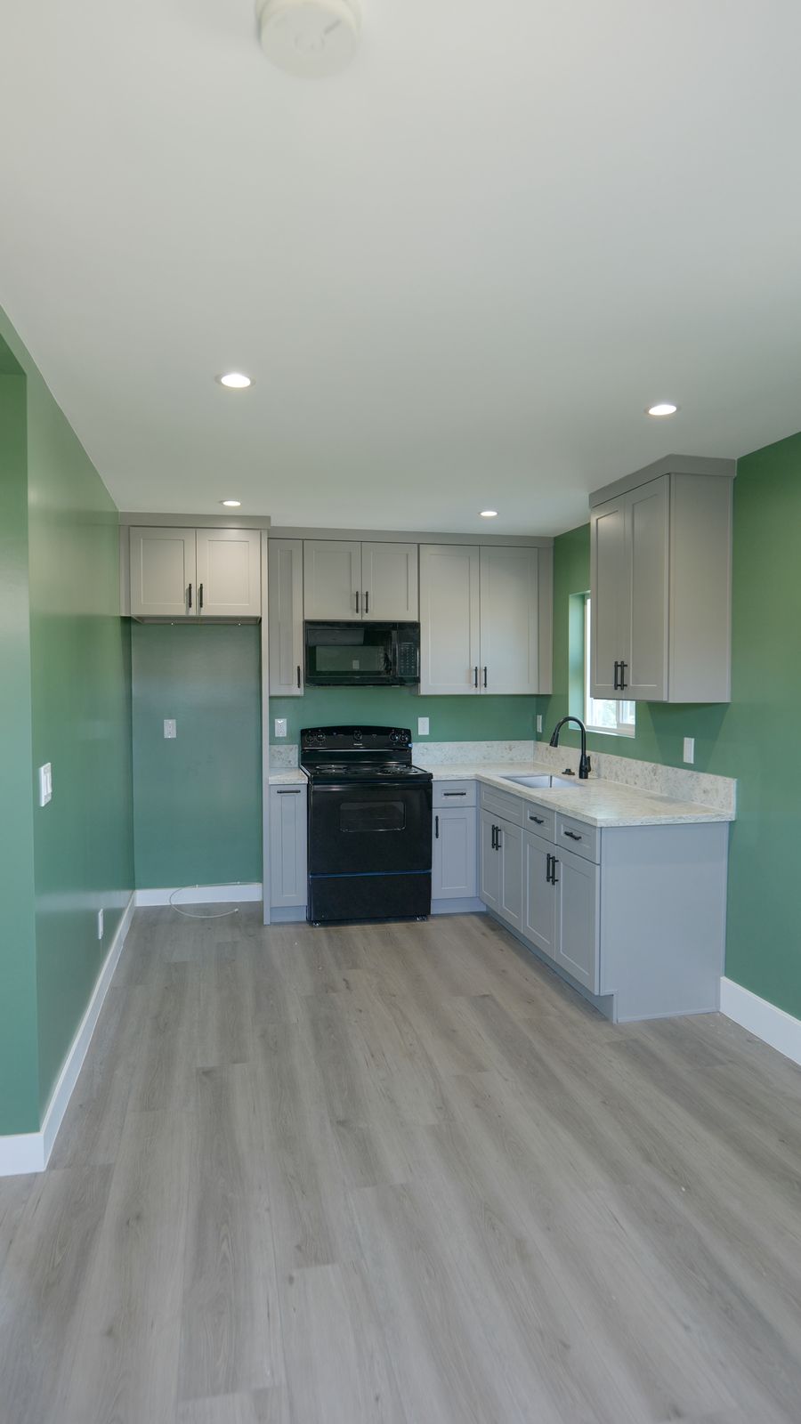 finished kitchen with white cabinets, black stove, microwave, green walls, and light wood flooring