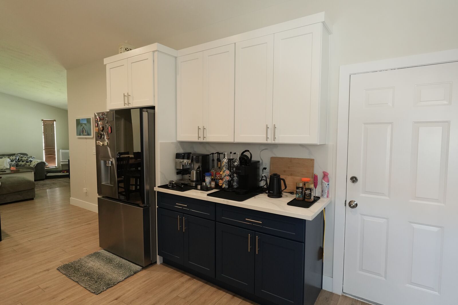 finished kitchen with white cabinets, dark lower cabinets, black refrigerator, and wood floor