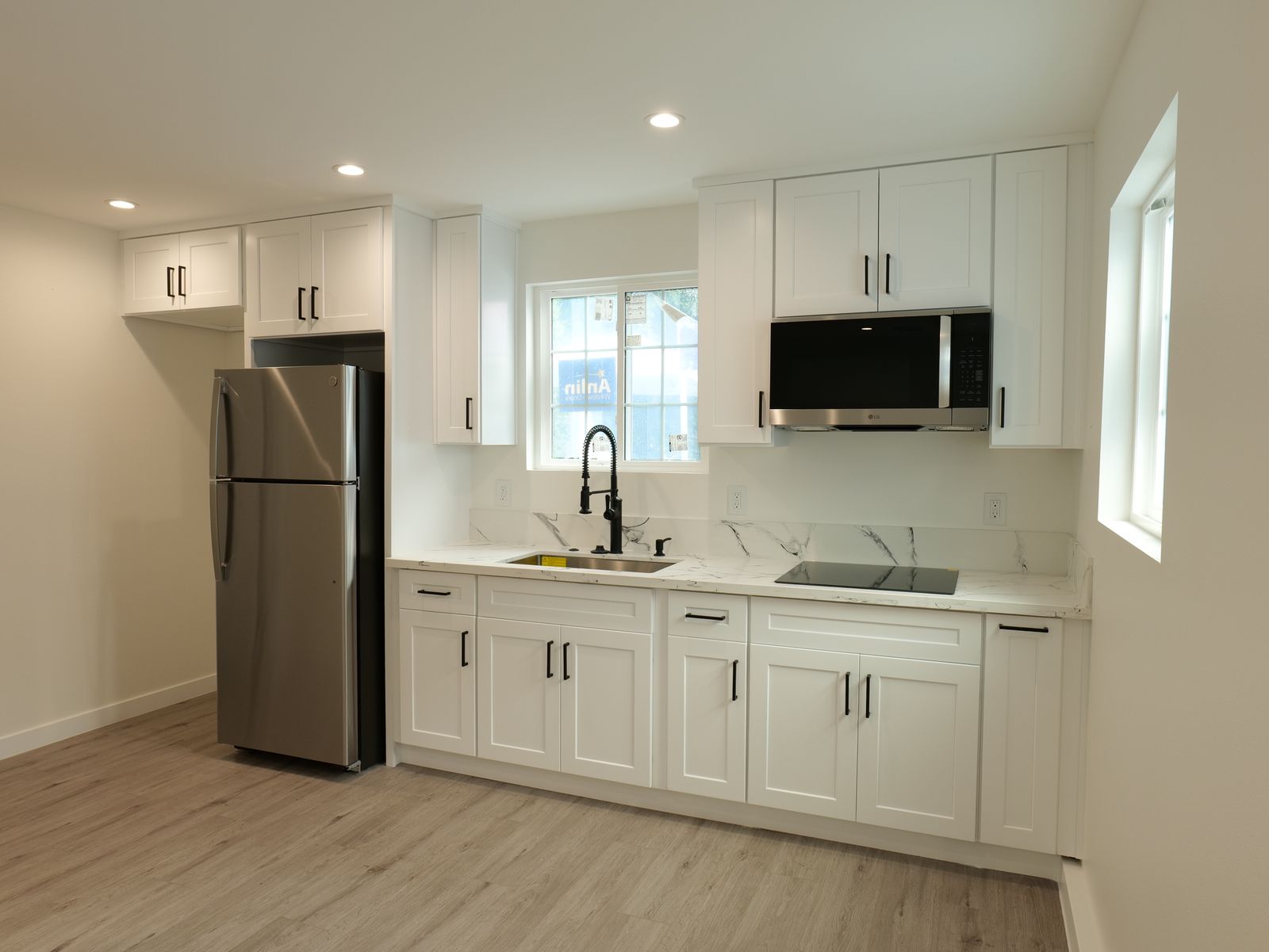 white kitchen view with stainless appliances, upper cabinets, sink, and bright window
