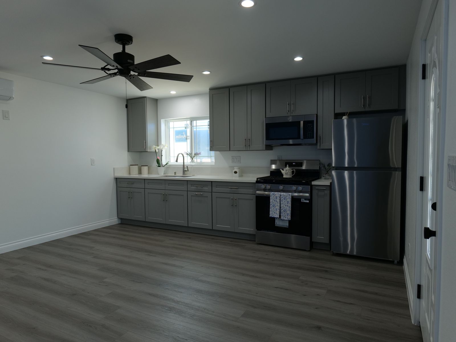 gray kitchen cabinets with stainless steel appliances, white countertop, island, and dark ceiling fan