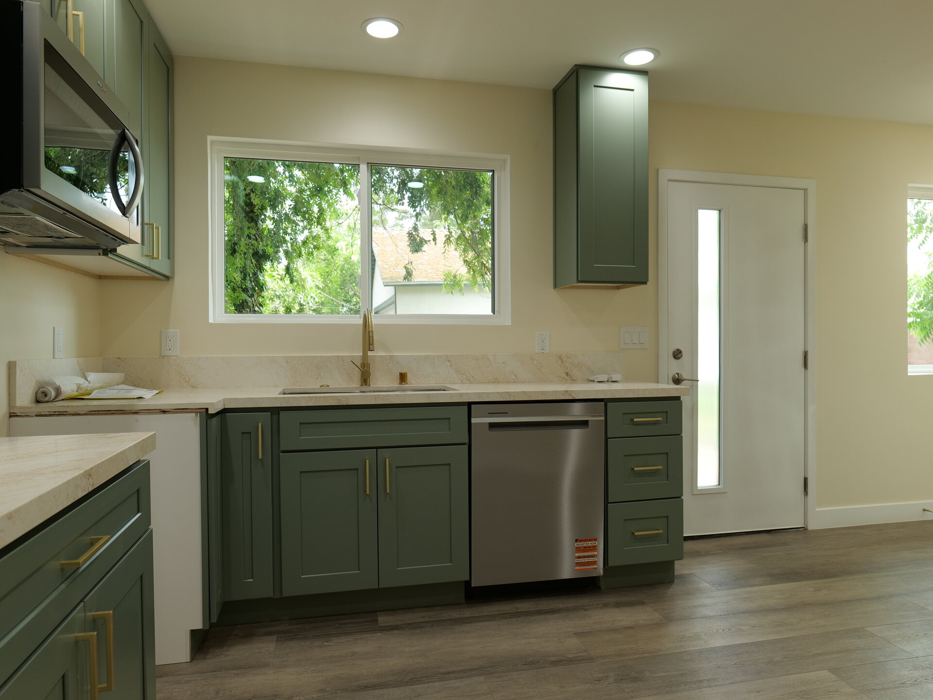 Sage green kitchen cabinets beneath a garden-facing window