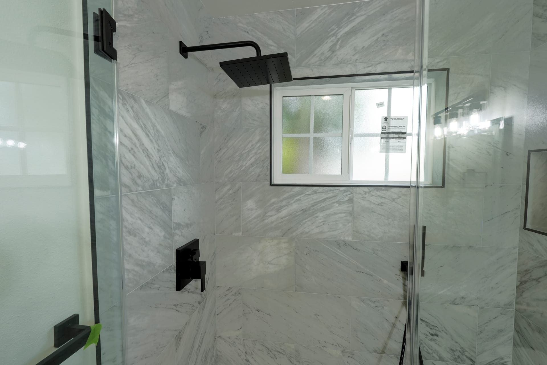 Glass-enclosed shower with marble-pattern tile and black fixtures