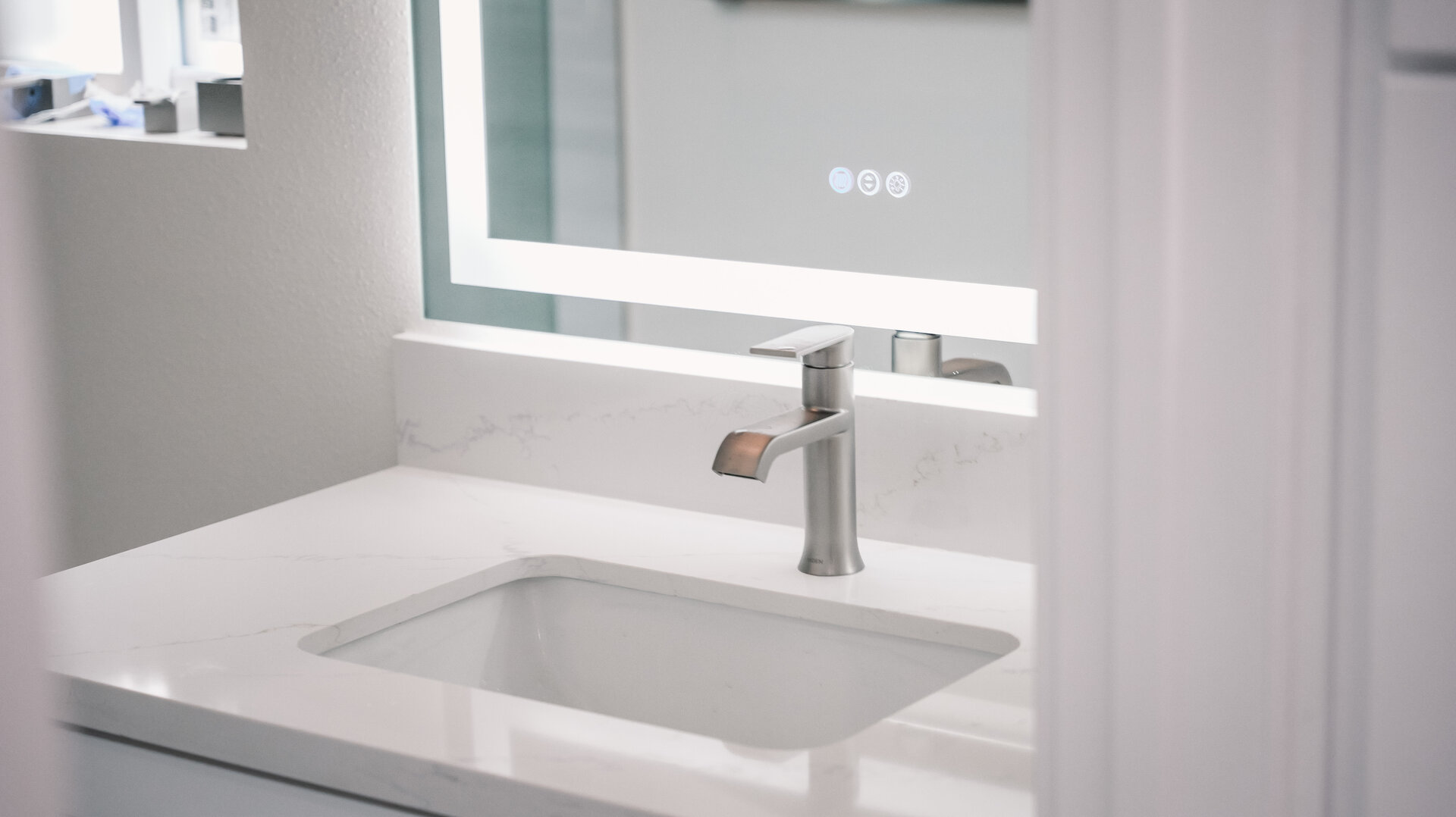 Bathroom sink and pale counter beneath a wide mirror
